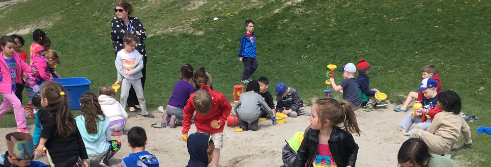 A class of younger students playing in the sand and grass.